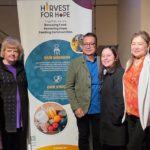Community members standing together beside a Harvest for Hope banner at the Surrey fundraiser supporting food rescue and local families.