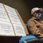 Surrey Speak – Photo from the CBC News town hall on Surrey’s extortion crisis, showing an audience member seated beside a large protest sign addressing safety and immigration concerns.