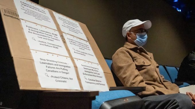 Surrey Speak – Photo from the CBC News town hall on Surrey’s extortion crisis, showing an audience member seated beside a large protest sign addressing safety and immigration concerns.
