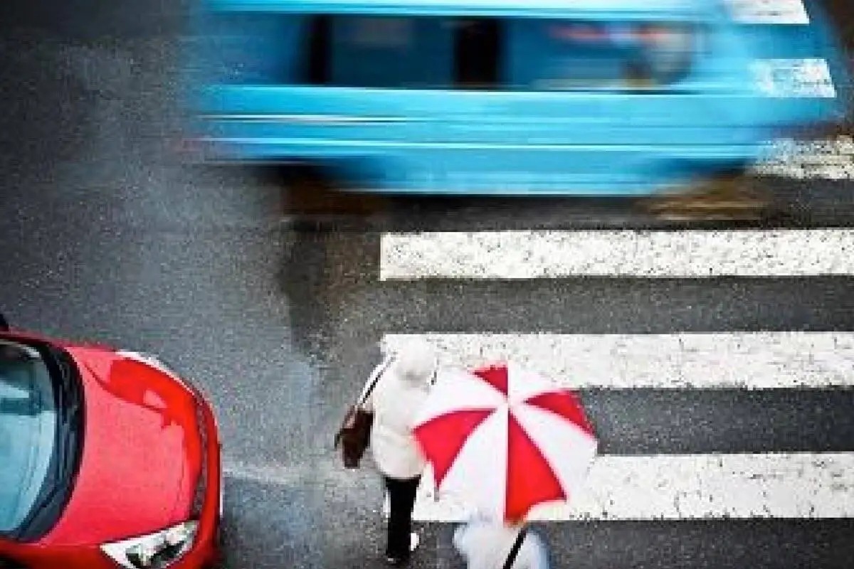 Surrey Speak – Pedestrians crossing a wet crosswalk with vehicles passing by, illustrating Surrey’s new speed limit reductions and Vision Zero pedestrian safety measures.