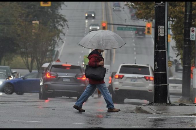 A pedestrian walking with an umbrella in rainy and windy Surrey weather as vehicles move through wet roads during a late November storm.
