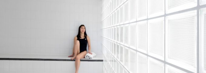 A woman in a black swimsuit relaxing in a bright steam room at a Surrey recreation facility, promoting winter wellness programs.