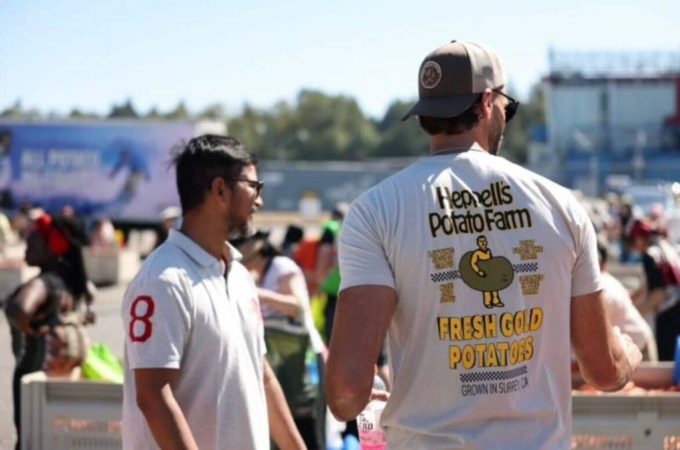 A volunteer wearing a Heppell’s Potato Farm shirt hands out potatoes during an Ugly Potato Day event in South Surrey, supporting food security and featured by Surrey Speak.