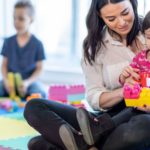Childcare worker helping a young child build with colourful blocks at a Surrey daycare offering 24/7 childcare for shift-working families.