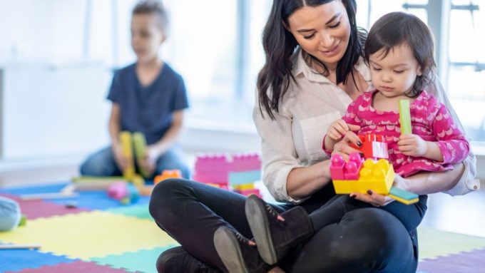 Childcare worker helping a young child build with colourful blocks at a Surrey daycare offering 24/7 childcare for shift-working families.