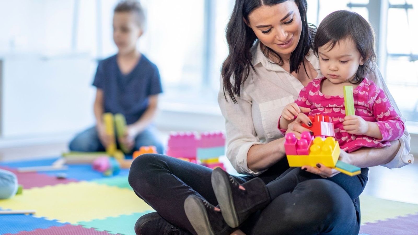 Childcare worker helping a young child build with colourful blocks at a Surrey daycare offering 24/7 childcare for shift-working families.