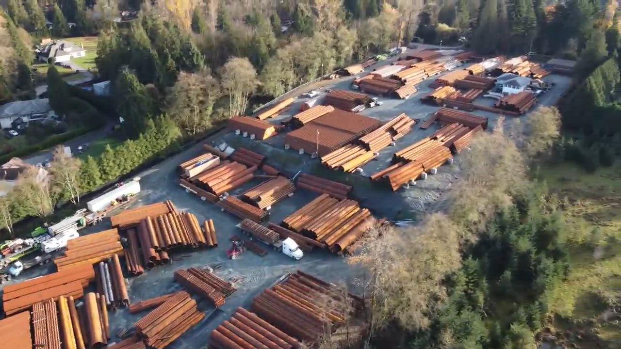 Aerial view of a Surrey industrial yard storing large steel pipes and materials, the site at the centre of a city injunction application over alleged bylaw violations.