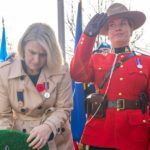 A person in formal attire lays a wreath beside an RCMP officer saluting during a public ceremony in B.C., used by Surrey Speak for coverage related to the Interpretation Act debate.
