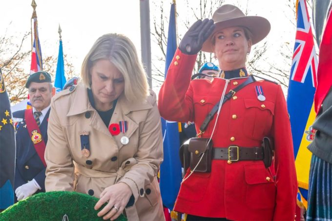 A person in formal attire lays a wreath beside an RCMP officer saluting during a public ceremony in B.C., used by Surrey Speak for coverage related to the Interpretation Act debate.