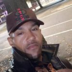 Man wearing a cap and leather jacket standing on a Surrey street at night, identified as Adam Troy Mann.