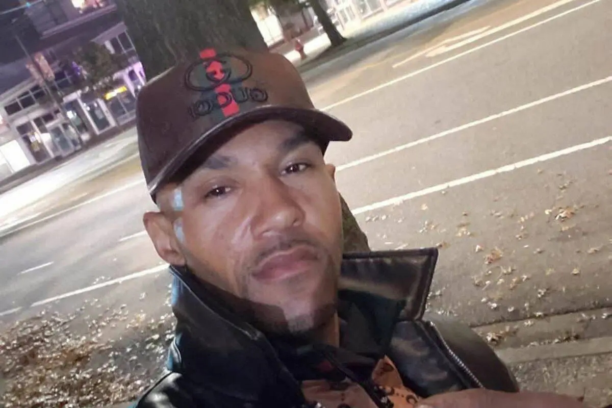 Man wearing a cap and leather jacket standing on a Surrey street at night, identified as Adam Troy Mann.