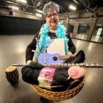 A woman stands in a studio holding a basket of yarn, a flute, a ukulele and other creative supplies that reflect the Artist Garage Sale in Surrey.