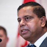 Close-up of Public Safety Minister Gary Anandasangaree speaking at a podium, with a blurred Canadian flag in the background.