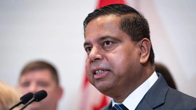 Close-up of Public Safety Minister Gary Anandasangaree speaking at a podium, with a blurred Canadian flag in the background.