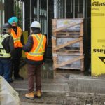 Three people in safety gear stand at a construction entrance discussing progress on the Guru Nanak Diversity Village long-term care facility in Cloverdale.