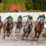 Thoroughbred horses and jockeys race around a muddy track curve at Hastings Racecourse, capturing the intensity of live horse racing in Vancouver.