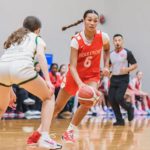 Holy Cross Crusaders player in a red jersey dribbles the basketball against a defender during a girls tournament game at Langley Events Centre.