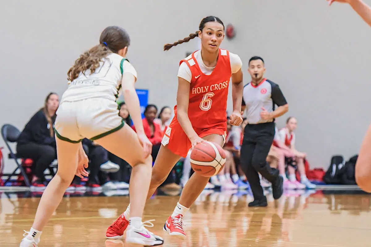 Holy Cross Crusaders player in a red jersey dribbles the basketball against a defender during a girls tournament game at Langley Events Centre.