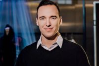 Portrait of teacher Lev Mihalik standing indoors in a dark sweater and collared shirt, winner of UBC’s 2025 Alumni Educator of the Year Award.
