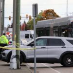 Police officers and a cruiser at a taped-off Surrey street beside a city bus after a collision.