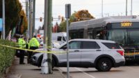 Police officers and a cruiser at a taped-off Surrey street beside a city bus after a collision.