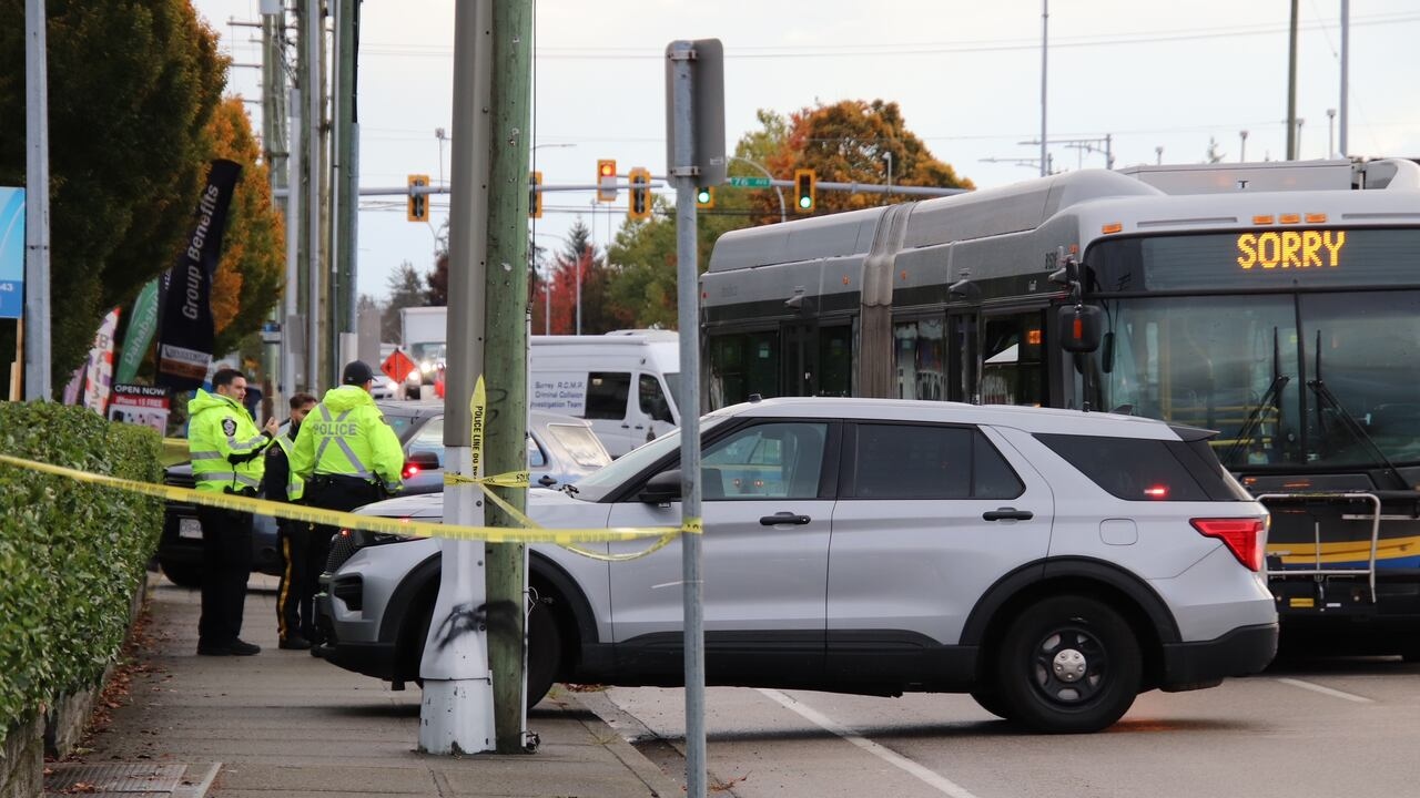 Police officers and a cruiser at a taped-off Surrey street beside a city bus after a collision.