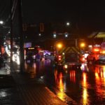 Emergency vehicles and police block a wet Surrey intersection at night after a shuttle bus collision.