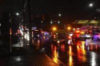 Emergency vehicles and police block a wet Surrey intersection at night after a shuttle bus collision.