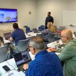 Business owners attending a hands-on AI training workshop at Surrey Libraries’ City Centre Branch, with a facilitator guiding them using laptops and a presentation screen.