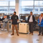 Business leaders tour a high-tech lab at Innovation Boulevard in Surrey, listening to a presenter explain advanced manufacturing and automation equipment.
