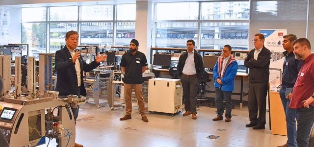 Business leaders tour a high-tech lab at Innovation Boulevard in Surrey, listening to a presenter explain advanced manufacturing and automation equipment.