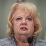 Surrey’s mayor speaks at a podium microphone, reacting to refugee claims made by suspects in B.C.’s extortion investigations.