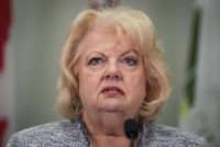 Surrey’s mayor speaks at a podium microphone, reacting to refugee claims made by suspects in B.C.’s extortion investigations.