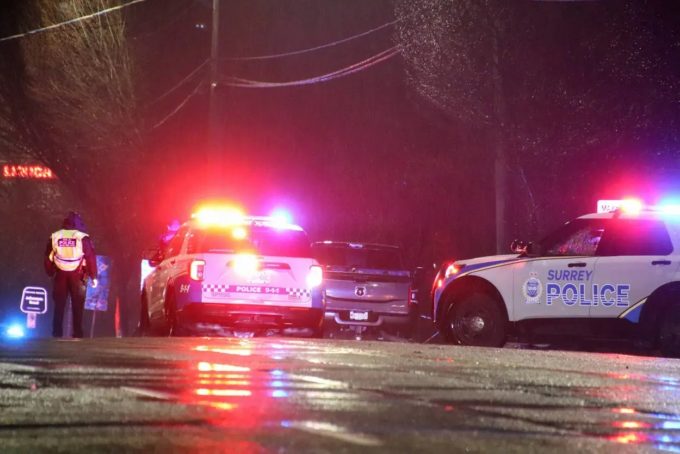 Surrey Police vehicles with flashing lights block a wet road at night as officers work at a collision scene.