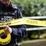 Surrey Police officer putting up yellow police tape at a roadside scene, representing a serious single-vehicle collision investigation in South Surrey.