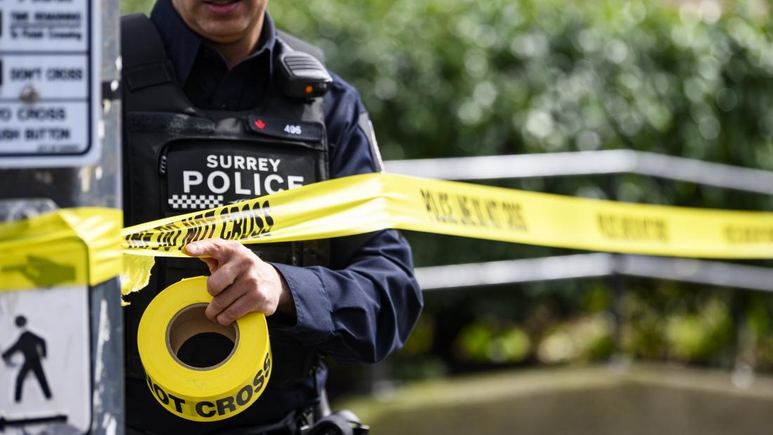 Surrey Police officer putting up yellow police tape at a roadside scene, representing a serious single-vehicle collision investigation in South Surrey.