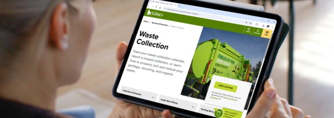 Person holding a tablet showing the City of Surrey waste collection webpage with options for chatting and pickup schedules.