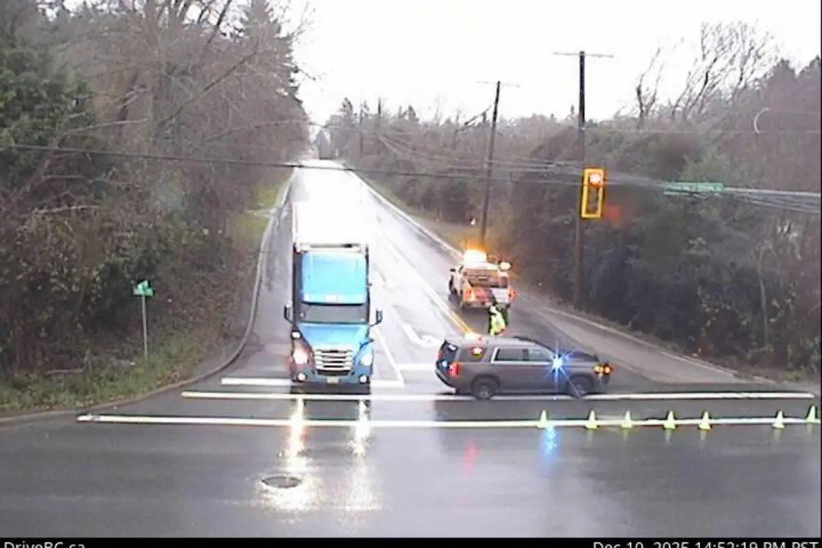 Traffic control vehicles block a wet section of 16 Avenue in South Surrey, with cones across the road after a tractor-trailer rollover.