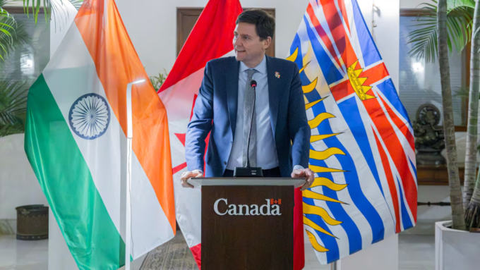 David Eby speaks during a trade mission event in India, with the flags of India, Canada and British Columbia behind him.
