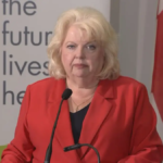 Surrey Mayor Brenda Locke speaks at a podium calling for federal action on extortion-related violence in Canada