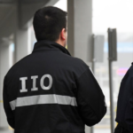 IIO investigator wearing a jacket marked “IIO” at an incident scene