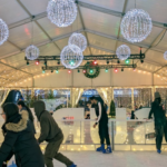 People enjoying free outdoor ice skating under a covered rink with festive lights at Surrey Civic Plaza during a winter event.