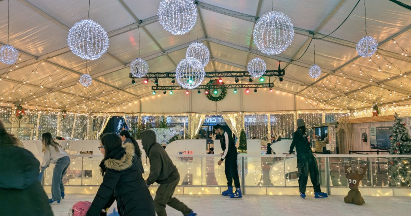 People enjoying free outdoor ice skating under a covered rink with festive lights at Surrey Civic Plaza during a winter event.