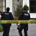 Surrey police officers walk near a taped-off residential area during an extortion-related investigation.