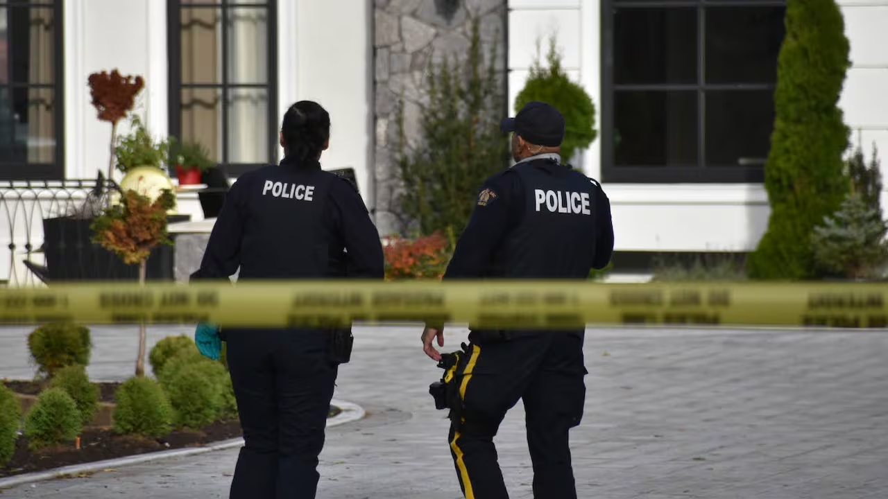 Surrey police officers walk near a taped-off residential area during an extortion-related investigation.