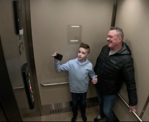 A young boy records an elevator ride on a smartphone while standing with his father inside an elevator in Surrey, B.C.