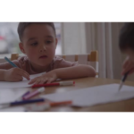 A boy sitting with a colored pencil in his hand