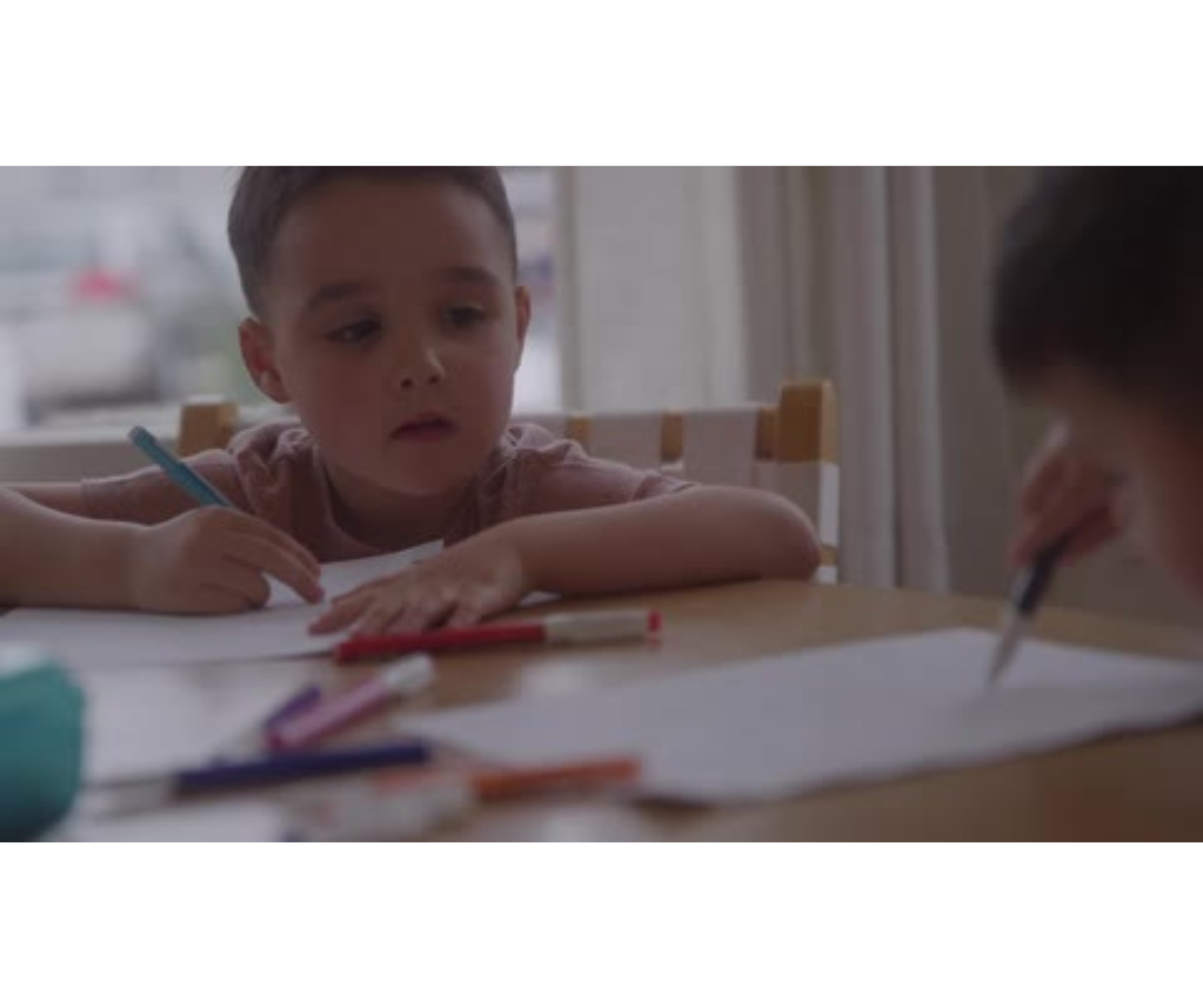 A boy sitting with a colored pencil in his hand