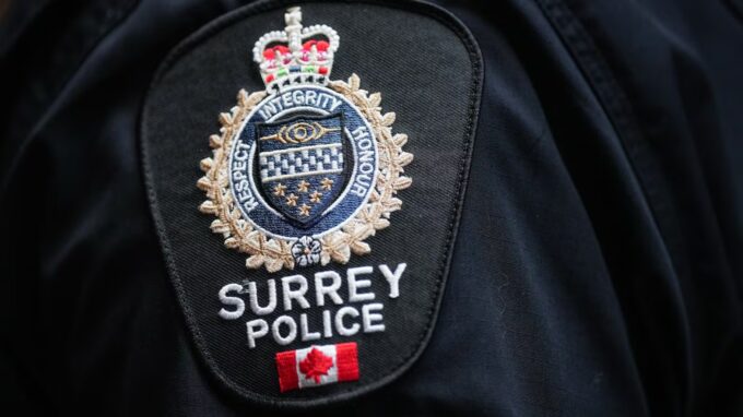 Police vehicles and officers at a nighttime residential crime scene in Surrey after a home was struck by gunfire.