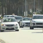Vehicles driving through a busy British Columbia roadway with parked cars nearby.
